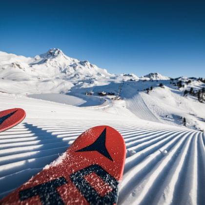 Red ski tips on freshly groomed slope in snowy alpine mountain landscape